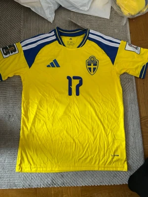 Svensk landslagströja Adidas gul/blå - Säljer en officiell svensk landslagströja från Adidas i storlek M. Tröjan är gul med blå detaljer, nummer 17 på bröstet och Sveriges landslagsemblem. Klassisk rund hals med blå och vita ränder på axlarna. Tillverkad i lätt och ventilerande material.