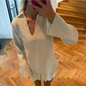 Beige ribbstickad tröja med krage - Säljer en beige ribbstickad tröja med v-ringad hals och breda ärmar. Tröjan har en avslappnad passform och en liten krage som ger en cool touch. Perfekt att styla med kjol eller jeans för en trendig look.