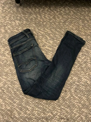 Mörkblå Replay jeans - Snygga mörkblå slimfit jeans från replay med klassisk femficksdesign och diskreta slitningar. Jeansen har en slim passform och coola detaljer på bakfickorna. Perfekta för dig som gillar en stilren och modern look. Storlek W31 L32
