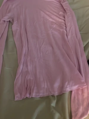 Ljusrosa långärmad topp - Säljer en enkel och stilren ljusrosa långärmad topp. Toppen har en rak passform och är tillverkad i ett mjukt, tunt material som känns skönt mot huden. Perfekt att matcha med jeans eller kjol för en avslappnad look.