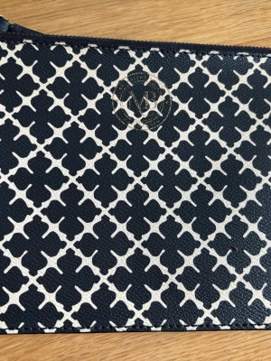 Svartvit kuvertväska By Malene Birger  - Kuvertväska med svart och vit grafiskt mönster från Laven. Väskan har en dragkedja upptill och är tillverkad i ett tåligt material med struktur. Perfekt för att bära småsaker och har en stilren design med diskret logotyp på framsidan.