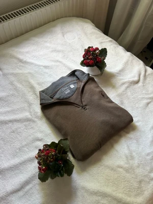 Brun halvzip tröja från Polo Ralph Lauren - Snygg brun tröja från Polo Ralph Lauren med halv dragkedja och klassisk krage. Tröjan har en diskret broderad logga på bröstet och är tillverkad i mjukt bomullsmaterial. Perfekt för en avslappnad men stilren look. Självklart äkta!