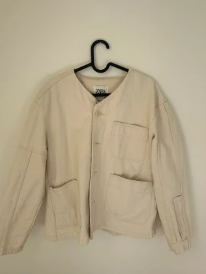 Beige jacna från Zara - Stilren beige jacka från Zara med tre stora fickor framtill och knappstängning. Jackan har en avslappnad passform och är tillverkad i ett kraftigare tyg. Perfekt för lager på lager och enkel att styla till olika looks.