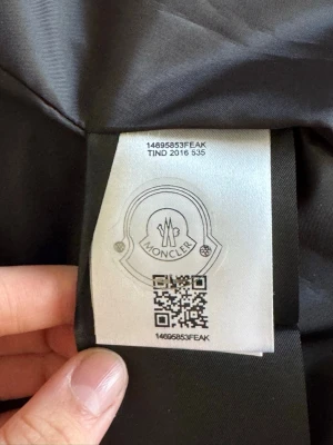 Svart dunjacka från Moncler - Snygg svart dunjacka från Moncler med klassisk quiltad design och glansig finish. Jackan har innerfoder med serietidningsmönster och detaljer som logotypmärke på insidan. Perfekt för kalla vinterdagar och riktigt trendig. Vid snabb affär kan vi diskutera pris