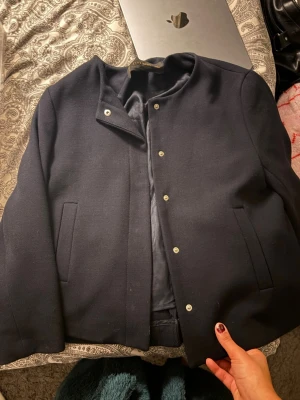Mörkblå jacka från Zara Basic - Stilren mörkblå kappa från Zara Basic med rak passform och tryckknappar framtill. Jackan har två diskreta sidofickor och en enkel, kraglös design som ger en clean look. Materialet är mjukt och fodrat för extra komfort:)❤️ storlek S