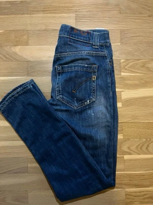 Blå raka dondup jeans med slitningar - Säljer ett par blå dondup jeans med raka ben och coola slitningar. Jeansen har klassisk femficksdesign, kontrastsömmar. Perfekta för en avslappnad och trendig look.