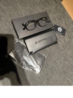 Svarta glasögon Chrome Hearts - Snygga svarta solglasögon från Chrome Hearts med klassisk rektangulär form. Bågarna är i svart och har silvriga detaljer vid gångjärnen. Kommer med originalfodral och putsduk. Perfekt accessoar för dig som vill sticka ut med stil.