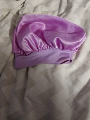 Ljuslila satin sovmössa - Snygg ljuslila sovmössa i glansigt satinmaterial. Mössan har en bred resårkant som håller den på plats under natten och skyddar håret mot friss. Perfekt för dig som vill vakna med mjukt och glansigt hår. Ingen synlig logga eller märke.