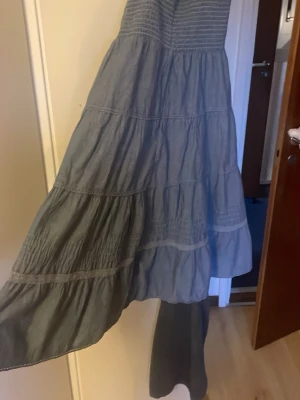 Grå långklänning med smock och volanger - Luftig söt klänning. Axelbanden är knutna lite konstigt på bilden men de är justerbara. Det står att den är storlek 36 men den är väldigt liten jag skulle säga att den är xs- xxs 