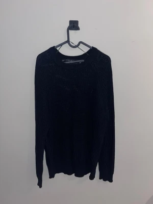 Svart stickad tröja med rund hals - En enkel och stilren svart stickad tröja med rund halsringning och långa ärmar. Tröjan har en rak passform och ribbade muddar vid ärmslut och nederkant. Perfekt att matcha med jeans eller kjol för en avslappnad look.