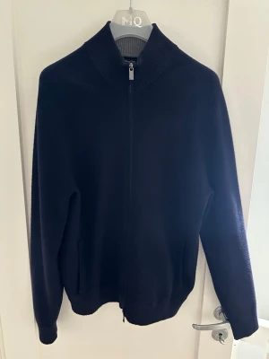Marinblå ziptröja från Massimo Dutti - Stilren marinblå ziptröja från Massimo Dutti med hög ribbad krage och hel dragkedja framtill. Tröjan har två fickor och är tillverkad i ett mjukt, stickat material som känns lyxigt och bekvämt. Den är riktigt riktigt skön och är i väldigt bra skick. STORLEK L MEN SKULLE SÄGA PASSAR ENDAST M.