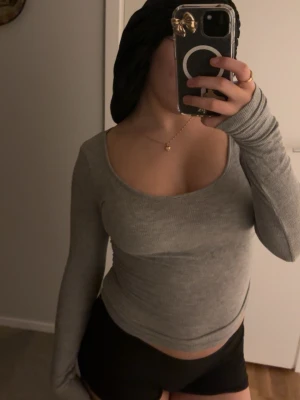 Grå ribbad långärmad topp - Säljer en grå ribbad långärmad topp med djup, rundad urringning. Toppen har en slim passform och är tillverkad i ett mjukt stretchigt material som sitter snyggt på kroppen. Perfekt att styla med både jeans och kjol.