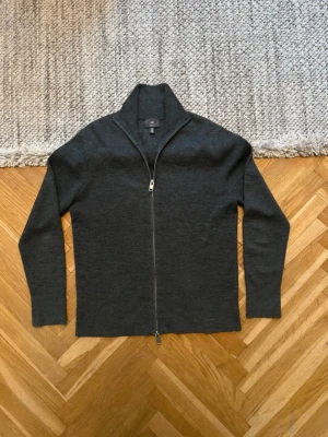 Mörkgrå ziptröja från H&M - Mörkgrå ziptröja från H&M med hög krage och hel dragkedja framtill. Tröjan är tillverkad i ett mjukt stickat material och har en stilren, rak passform med långa ärmar. Perfekt för lager-på-lager och enkel att matcha med olika outfits.