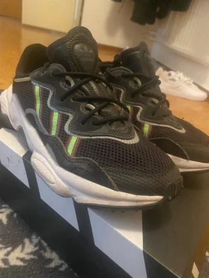 Adidas svarta sneakers med färgglada detaljer - Svarta Adidas sneakers med mesh- och mockadetaljer, vita sulor och färgglada ränder i grönt och rött på sidorna. Skorna har en chunky design och svarta skosnören. Perfekta för dig som gillar streetwear och vill sticka ut lite extra.