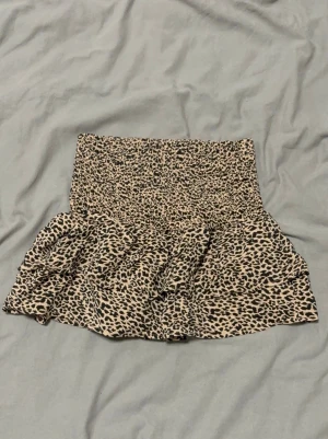 Leopardmönstrad skort med volang - Supersnygg leopardmönstrad skort med bred smock i midjan och volangig kjoldel. Skorten har inbyggda shorts under kjolen och är gjord i ett mjukt, stretchigt tyg. Perfekt för dig som vill ha både stil och komfort i ett plagg.