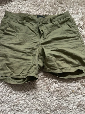 Olivgröna shorts från 157 - Snygga olivgröna shorts från 157 med klassisk passform och bälteshällor. Tillverkade i mjuk bomull, perfekta för varma dagar. Två sidofickor och enkel design gör dem lätta att matcha med olika stilar.