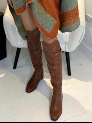 Bruna knähöga stövlar i skinn, 35 - Snygga bruna knähöga stövlar i skinn med rundad tå och dekorativt spänne på sidan. Stövlarna har en klassisk design och passar perfekt till både kjol och jeans. De har en liten klack och är lätta att matcha med olika outfits.