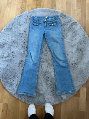 Ljusblå bootcut jeans med fickor - Snygga ljusblå jeans med bootcut passform och klassiska fem fickor. Jeansen har dubbla knappar framtill och en extra ficka med lock. Perfekta för dig som gillar en retro vibe och vill ha ett par jeans som sticker ut lite extra.