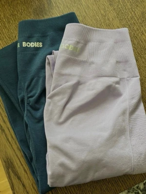 Seamless leggings från Better Bodies - Två par seamless leggings från Better Bodies, ett par i ljuslila och ett par i turkosblå. Båda har hög midja och är tillverkade i ett stretchigt material som sitter tajt och bekvämt. Perfekta för gymmet eller annan träning. Diskret logga i midjan.