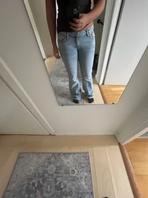 Ljusblå bootcut jeans - Säljer ett par ljusblå bootcut jeans med klassisk femficksdesign och normal midja. Jeansen har en snygg tvätt och är tillverkade i ett mjukt denimtyg som sitter skönt. Passar perfekt till sneakers eller boots för en avslappnad look.