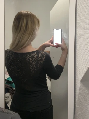 Svart topp med spetsdetaljer - Snygg svart topp med v-ringning och trekvartsärm. Baksidan har genombruten spets som ger en elegant touch. Toppen är figurnära och passar perfekt till jeans eller kjol.