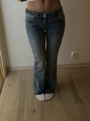 Blå bootcut jeans med låg midja - Säljer ett par klassiska blå bootcut jeans med låg midja och fem fickor. Jeansen har en snygg tvättad look och stängs med knapp och dragkedja. Perfekta för en avslappnad och trendig stil. Hör av er vid frågor! Levererar så fort jag kan!!