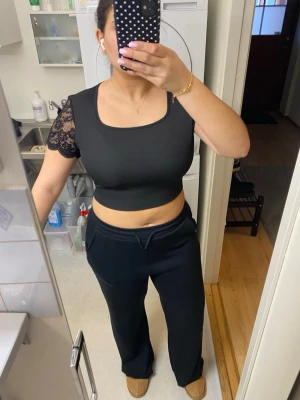 Svart croppad topp med spets och öppen rygg - Säljer en svart croppad topp med spetsdetaljer på ärmarna och öppen rygg med knytband. Toppen har en fyrkantig halsringning och är tillverkad i ett stretchigt material som sitter tight. Perfekt för dig som vill ha en unik och snygg look. Aldrig använd men ingen prislapp kvar.