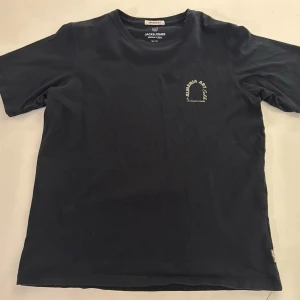 Svart t-shirt Jack & Jones med tryck - Svart t-shirt från Jack & Jones med coolt tryck på ryggen som föreställer en konstnärlig vy och texten 'ALMERIA ART Exhb.'. Rund halsringning och korta ärmar. Perfekt för dig som gillar streetstyle och grafiska prints.