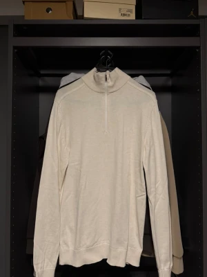 Beige halvzip tröja - Stilren beige tröja med halvzip och hög krage. Långärmad modell i mjukt material, perfekt för lager på lager. Enkel och clean design utan synliga loggor eller mönster.