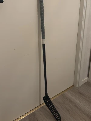 Svart innebandyklubba med grått grepp - Säljer en svart innebandyklubba med grått lindat grepp och plastblad. Skaftet är rakt och bladet har en tydlig böj för bättre bollkontroll. Perfekt för dig som gillar innebandy och vill ha en enkel men funktionell klubba. 