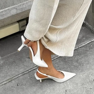 Vita pumps med spetsig tå och låg klack - Stilrena vita pumps med spetsig tå och öppen häl. Skorna har en smal rem runt hälen och en elegant låg klack. Perfekta för dig som vill ha en clean och modern look. Tillverkade i syntetmaterial med slät finish.