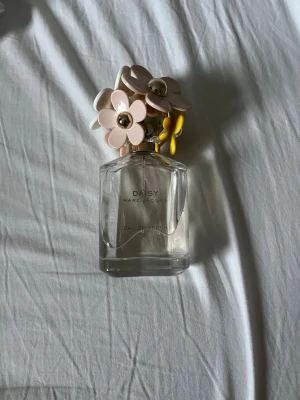 Daisy Eau So Fresh parfym Marc Jacobs - Daisy Eau So Fresh från Marc Jacobs är en söt parfym i en genomskinlig glasflaska med ett unikt lock dekorerat med rosa, vita och gula blommor i plast och gulddetaljer. Flaskan har en modern, feminin design som verkligen sticker ut på sminkbordet. Ursprungligen innehöll flaskan 75 ml men mer än hälften finns fortfarande kvar!! Har tyvärr inte kvar original kartongen men kommer att slå in den säkert vid post💕
