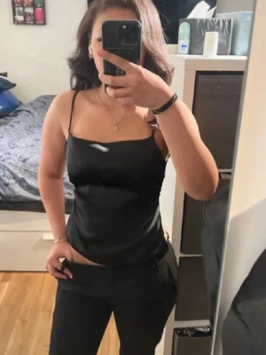 Svart satin linnetopp med rosett - Snygg svart linnetopp i satin med smala axelband och stor rosett baktill. Toppen har en croppad passform och öppen rygg, perfekt för att skapa en cool och trendig look.