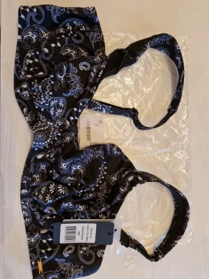 Svart bikini med paisleymönster - Snygg svart bikini från Change med vitt paisleymönster. Överdelen är storlek 90B med axelband som kan ändras och under delen är storlek 48 av en högre model. Bikinin är provad men aldrig använd och prislapparna finns kvar. 