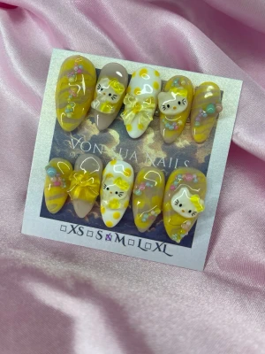 LemonKitty (M);Medium Almond - Supergulliga handgjorda press-on naglar i gult och vitt med 3D-dekorationer, söta HK kattmotiv och rosetter. Mix av randigt och prickigt. Medium Långa, mandelformade naglar som verkligen sticker ut och ger en lekfull vibe.M: 16 mm, 12 mm, 12,5 mm, 11,5 mm, 10 mm