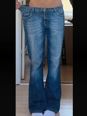 Blå bootcut jeans med broderade fickor - Säljer ett par blå bootcut jeans med snygg slitning och broderade detaljer på bakfickorna. Jeansen har klassisk femficksmodell och är tillverkade i denim. Perfekta för dig som gillar en avslappnad men trendig look.