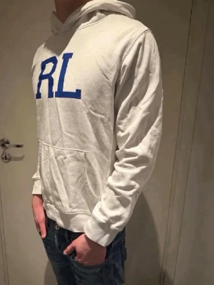 Vit hoodie från Ralph Lauren🤩🙌 - Säljer en vit hoodie från Ralph Lauren med stort blått RL-tryck på bröstet. Hoodien har huva, ribbade muddar och en klassisk magficka. Perfekt för dig som gillar stilrena och sportiga plagg. Materialet är mjukt och bekvämt.🤩🙌