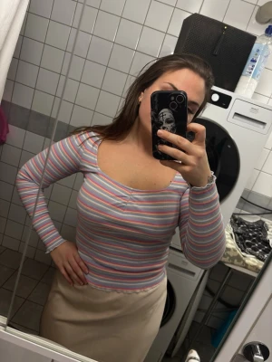 Randig långärmad topp - Säljer en långärmad topp med v-ringning och smal passform. Toppen har ett färgglatt randigt mönster i rosa, blått, vitt och grått. Perfekt för dig som gillar en enkel men färgstark stil.