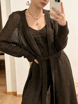 Marimekko Brun lång kofta från Marimekko - Snygg lång kofta i brun, transparent stickning från Marimekko. Koftan har ett knytband i midjan, långa ärmar och en avslappnad passform. Perfekt att slänga över en topp eller klänning för en cool lager-på-lager-look.