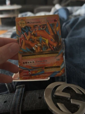 Pokémonkort Mega Charizard EX - Säljer ett Pokémonkort med Mega Charizard EX-motivet. Kortet har en färgstark design med orange och blå detaljer samt japansk text. Det är tillverkat av papper och har Crimson Drive-attacken med 300 HP.