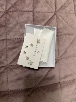 Söta silvriga örhängen med fjärilar - Set med små silvriga örhängen i olika former, bland annat stjärnor och fjärilar. Örhängena har en glittrig finish och är perfekta för att mixa och matcha. Kommer på ett smyckeskort och i en liten ask. Materialet ser ut att vara metall med strassdetaljer.