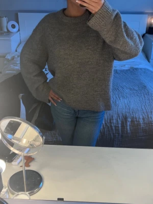 Grå oversized stickad tröja - Mysig grå stickad tröja med oversized passform och rund hals. Tröjan har långa ärmar och ribbade muddar vid ärmslut och nederkant. Perfekt för lager på lager och chill vardagsstil.