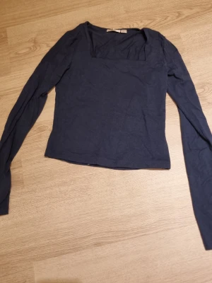 Mörkblå långärmad topp med fyrkantig ringning - En stilren mörkblå topp med lång ärm och fyrkantig ringning. Toppen har en slim passform och är tillverkad i mjuk bomull, perfekt för att matcha med jeans eller kjol. Enkel och trendig design som passar till många olika looks.