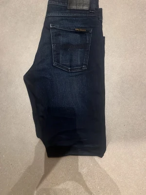 Mörkblå Nudie Jeans  - Snygga mörkblå jeans från Nudie med klassisk femficksmodell och raka ben. Jeansen har subtila slitningar och en liten logotyp på bakfickan. Modellen är lean Dean och passar i storleken w29 l30 men är i samma längd som ett par l32. Hör av er vid minsta fundering om jeansen. 😃