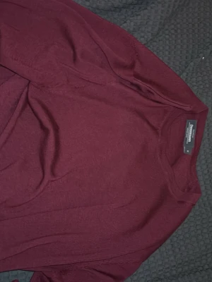 Vinröd merinoullströja Dressmann - Vinröd tröja från Dressmann i mjuk merinoull. Klassisk rund halsringning och långa ärmar. Perfekt för dig som gillar stilrena och bekväma plagg med enkel design.