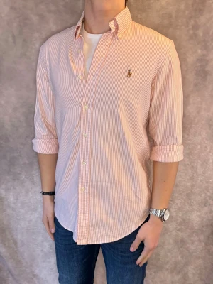 Randig Ralph Lauren Skjorta - Stl S - RIKTIGT FET RL SKJORTA I RANDIGT MÖNSTER MED FÄRGERNA APRIKOS OCH VIT, perfekt till sommaren som närmar sig! 🏖️🌊 | Mycket bra skick: 9,5/10, utan defekter! | Stl: S |  Modellen är 176cm och väger 75kg,  | Hör av dig vid frågor // Galgen 🫡