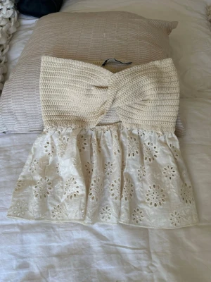 Beige virkad bandeau topp - Supersöt bandeau topp i beige med virkad överdel och broderad, utsvängd nederdel med blommönster. Toppen är axelbandslös och perfekt för sommardagar. Ger en bohemisk och trendig vibe.
