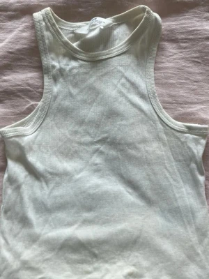 Vit ribbad linnetopp - Säljer en enkel och stilren vit ribbad linnetopp med rund halsringning. Toppen är ärmlös och har en klassisk passform som passar till det mesta. Perfekt att matcha med jeans eller kjol för en clean look.