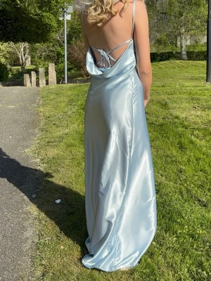 Ljusblå balklänning med öppen rygg - Säljer en ljusblå balklänning i satinliknande material. Klänningen har tunna axelband, öppen rygg med snörning och en snygg drapering baktill. Perfekt för dig som behöver klänning till balen i vår😊