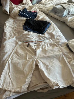 Vita shorts med fickor - Säljer ett par klassiska vita shorts. De har normal passform, sidofickor och bakfickor med knapp. Perfekta för sommaren och tillverkade i mjuk bomull för en skön känsla. Stängs med dragkedja och knapp framtill.